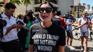 A woman with light-toned skin wears sunglasses and a shirt reading "DONALD TRUMP DID NOTHING WRONG!"