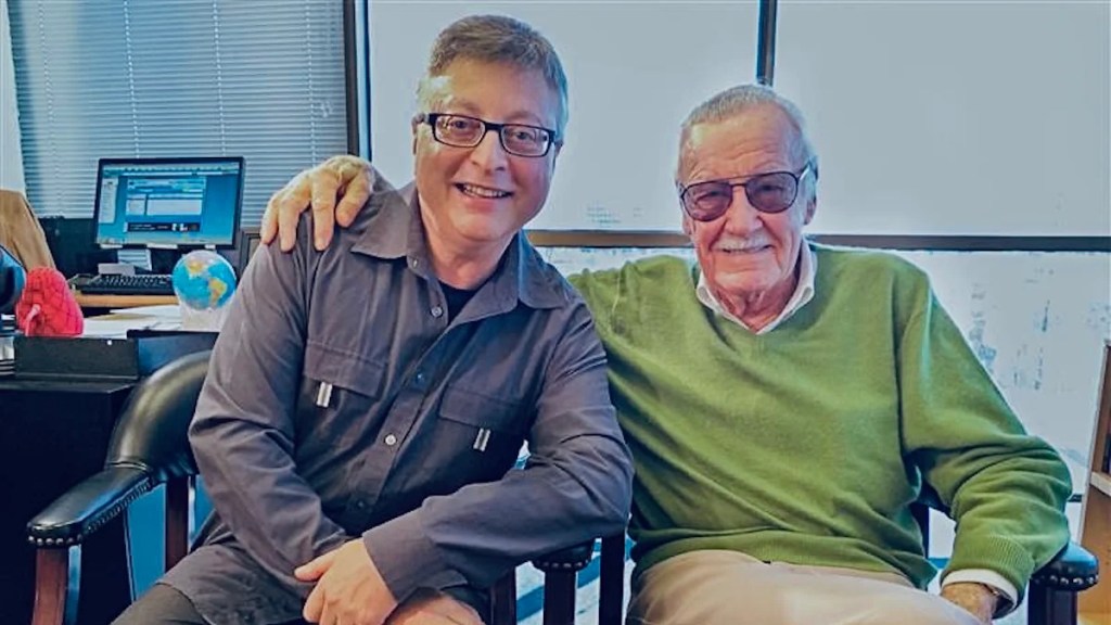 A pair of men with light-toned skin sit, the older one with his arm around the other.