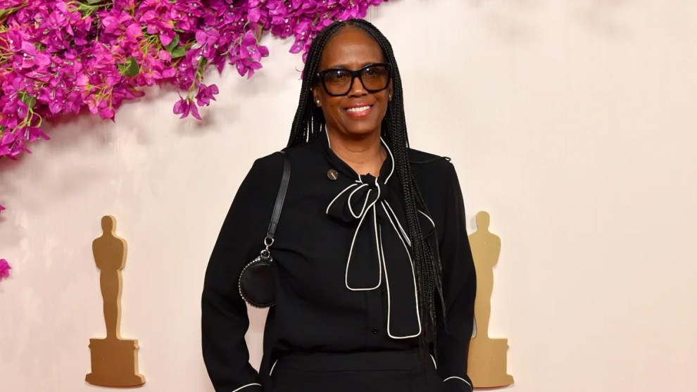 Kim Taylor-Coleman poses in front of a backdrop with pink flowers and small golden Oscars logos at the 96th Annual Academy Awards