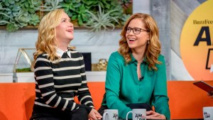 Angela Kinsey and Jenna Fischer, co-hosts of the Office Ladies podcast and former stars of The Office, sit on an orange couch during an interview