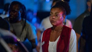 Taraji P. Henson stands solemnly in a tense nighttime scene from Netflix’s Straw, wearing a red volunteer vest over a white shirt, surrounded by a blurred crowd under dramatic blue and red emergency lights.